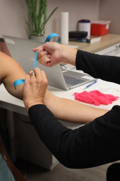 Medical professional using a tourniquet for drawing blood indoors.