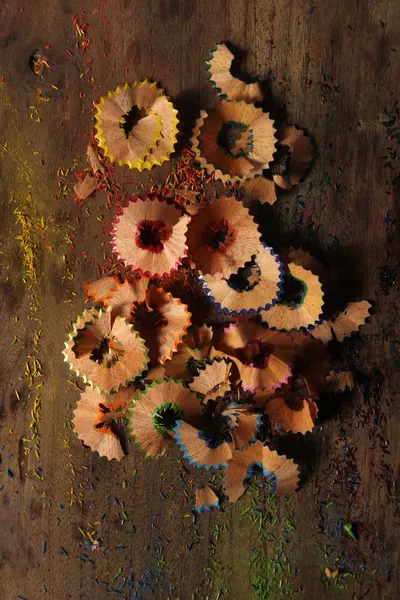 Colorful pencil shavings scattered on wooden surface, creating an artistic pattern.