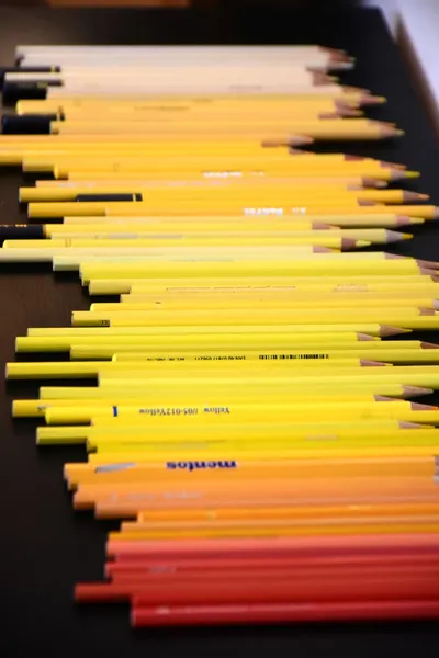Vibrant flat lay of numerous yellow and orange colored pencils on a dark surface.