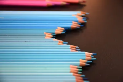 Array of blue colored pencils sharply aligned on a dark surface.