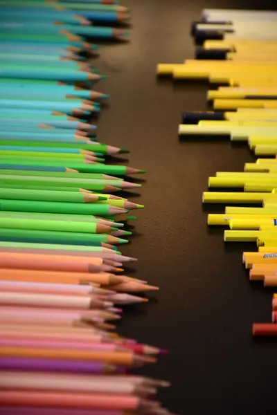 Brightly colored pencils and pens organized on a dark background, creating a vivid contrast.