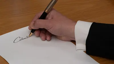 A professional signing a business contract with a fountain pen on a wooden desk.