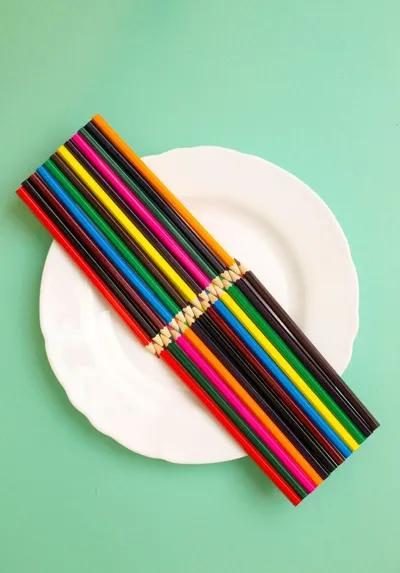 Colorful pencils arranged on a white plate against a teal background, creating a playful artistic composition.