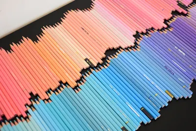 Brightly colored pastel pencils arranged in an artistic rainbow pattern on a black background.