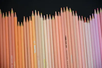 An array of pastel-colored pencils neatly arranged on a dark background.