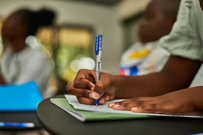Focused hand writing in notepad during a classroom study session.