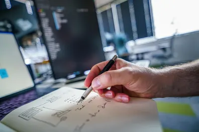 Close-up of a hand writing notes in a notebook with blurred office background. Perfect for business and productivity themes.