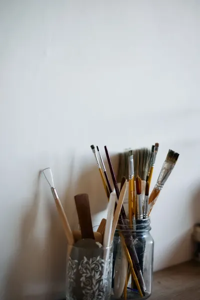 A collection of various paintbrushes in jars against a neutral wall.