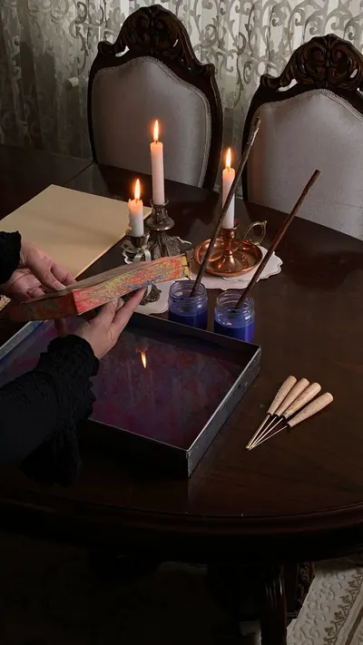Artist creating Ebru art with candles and tools on a dark wooden table. Warm and artistic ambiance.