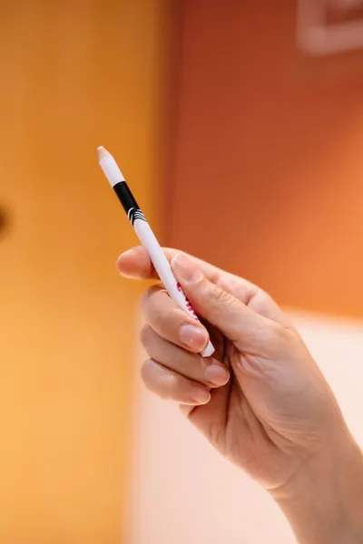 Close-up of a hand holding a white marker pen against an orange background, perfect for office or creative themes.