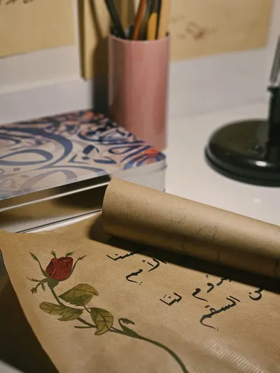 A cozy workspace featuring Arabic calligraphy and a delicate rose illustration, perfect for creative inspiration.