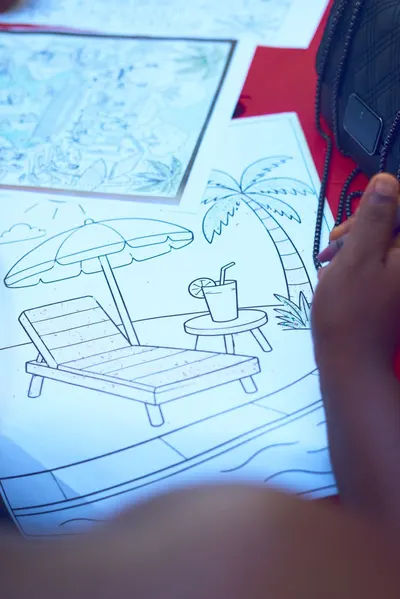 Child coloring a beach-themed illustration with umbrella and palm tree.
