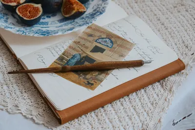 A vintage notebook with a pen and figs placed on a lace tablecloth, creating a classic still life.
