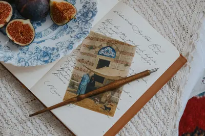 A vintage notebook with handwritten notes, figs on a plate, and an ink pen in a cozy setting.