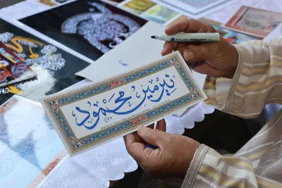 Close-up of hands holding an Arabic calligraphy piece on a decorative card.