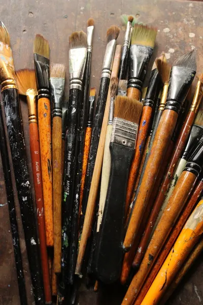 A collection of used paintbrushes lies on a rustic wooden table, showcasing artistic tools.