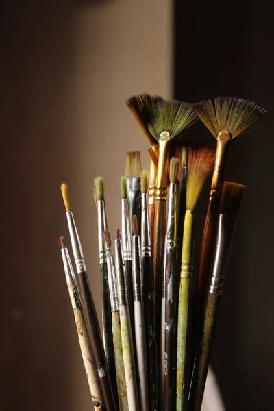 An assortment of artist paint brushes in warm indoor lighting, showcasing different styles.