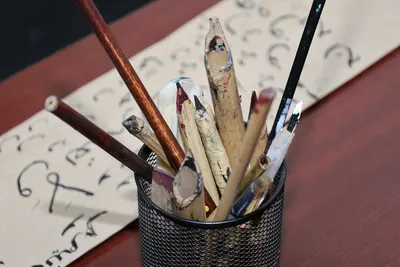 An artistic collection of pencils and brushes in a holder, set against calligraphy paper.