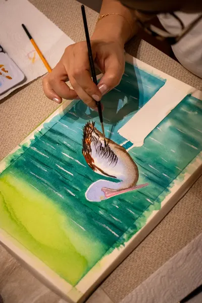 An artist meticulously paints a pelican in watercolor, showcasing skill and creativity.