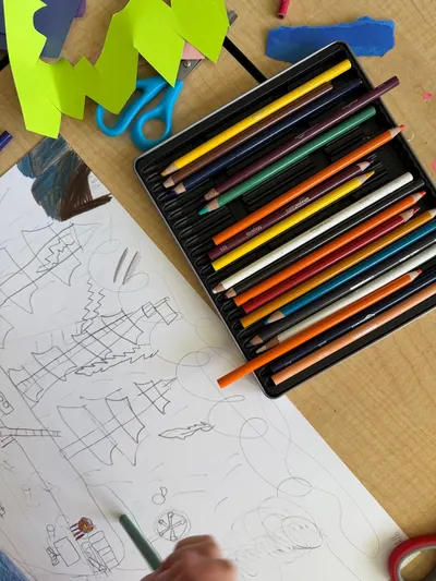 A creative scene with colored pencils and a child's hand drawing on paper.