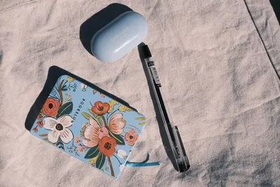 Flat lay of a colorful floral notebook, pen, and Samsung case on a fabric surface, capturing a modern lifestyle.
