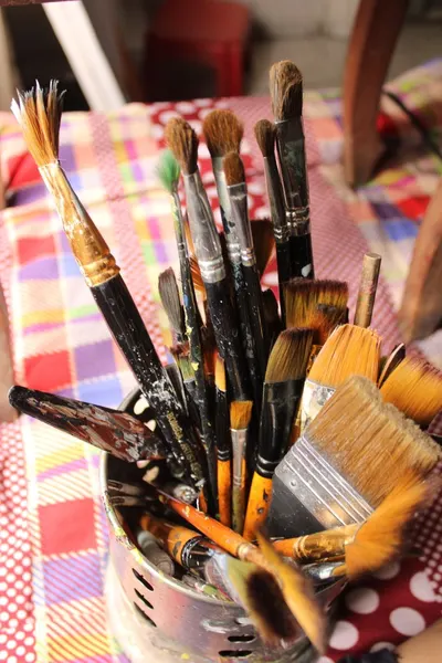 A diverse collection of paintbrushes in a holder on a vibrant checkered tablecloth.