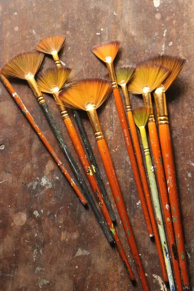 Artistic arrangement of fan brushes with colorful bristles on a rustic wooden table.