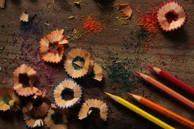 Artistic arrangement of vibrant pencil shavings and colored pencils on a rustic wood background.