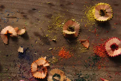 Close-up of vibrant pencil shavings spread across a wooden table, showcasing various colors.