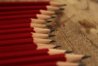 Neatly sharpened red pencils perfectly aligned on a wooden surface, showcasing symmetry and precision.
