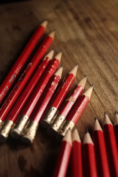 A collection of red pencils neatly arranged on a rustic wooden table, offering a warm artistic vibe.