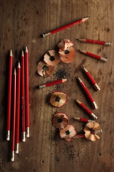 A collection of red pencils with shavings scattered creatively on a wooden table.