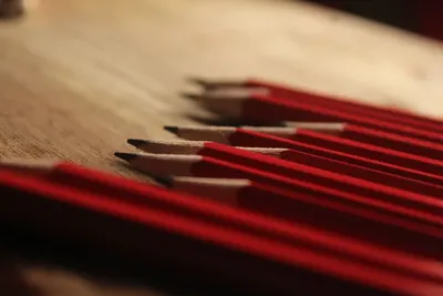 Close-up photo of sharpened red pencils aligned on a wooden table.