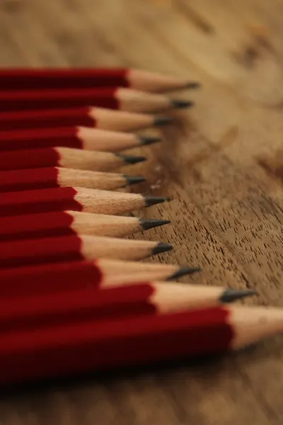 Red pencils arranged in a row on a wooden table, emphasizing texture and craft.