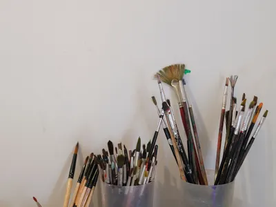 Close-up of various paintbrushes set in holders against a white wall in an artist's workspace.