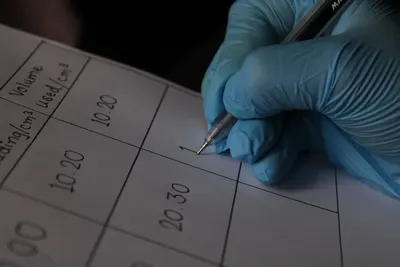 Close-up of a scientist wearing blue gloves writing measurements on a data sheet.