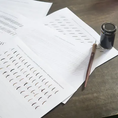 Calligraphy practice sheets with a dip pen and ink on a wooden table, perfect for beginners.