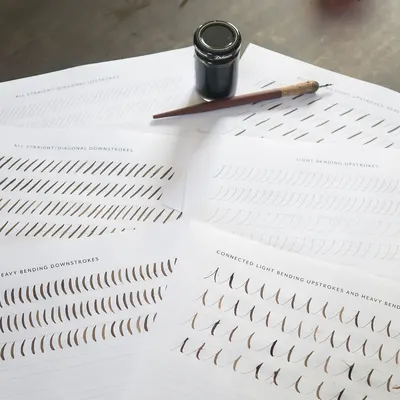 Overhead view of calligraphy practice sheets with an ink bottle and pen.