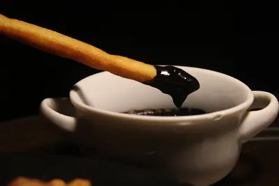 A crispy churro dipped in rich dark chocolate sauce in a white bowl.
