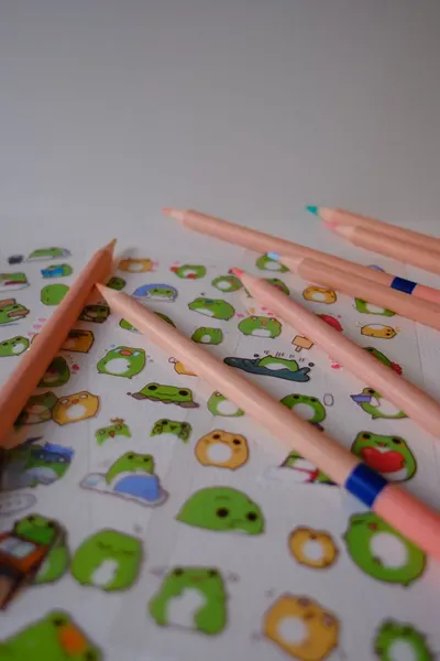 Pink pencils and cute frog stickers on a white background for creative projects.