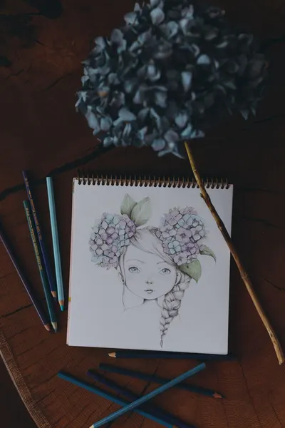 Artistic sketch of a girl adorned with hydrangeas, surrounded by colored pencils. Perfect for art themes.