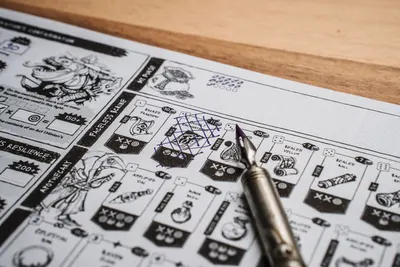 Close-up view of a vintage board game sheet with an ink fountain pen. Marks and drawings create an engaging tabletop scene.
