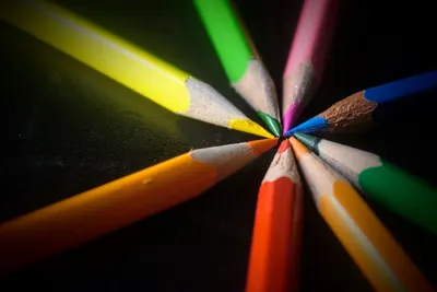 Vibrant colored pencils neatly arranged to form a circular pattern on a dark background.