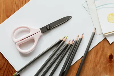 Top view of scissors and pencils placed over piece of paper and various patterns devoted for handmade art and creation