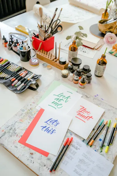 Top view of a creative calligraphy workstation with pens, inks, and vibrant lettering on paper.