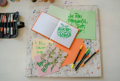 Flat lay of colorful calligraphy tools and artistic project on a desk.