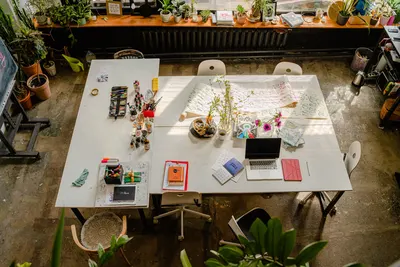 Aerial view of a bright, creative workspace featuring art supplies, plants, and a laptop.