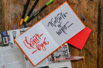 Explore creative calligraphy with vibrant art supplies and sketchbooks on a rustic wooden desk.