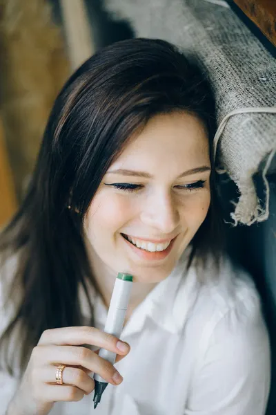 A cheerful woman in a white shirt smiles while holding a marker, showcasing her carefree attitude.