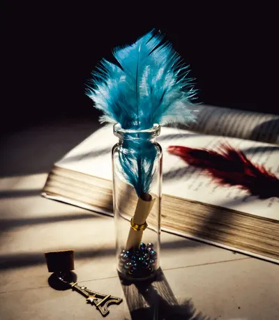 Blue feather in glass bottle arranged on shabby table with old opened book